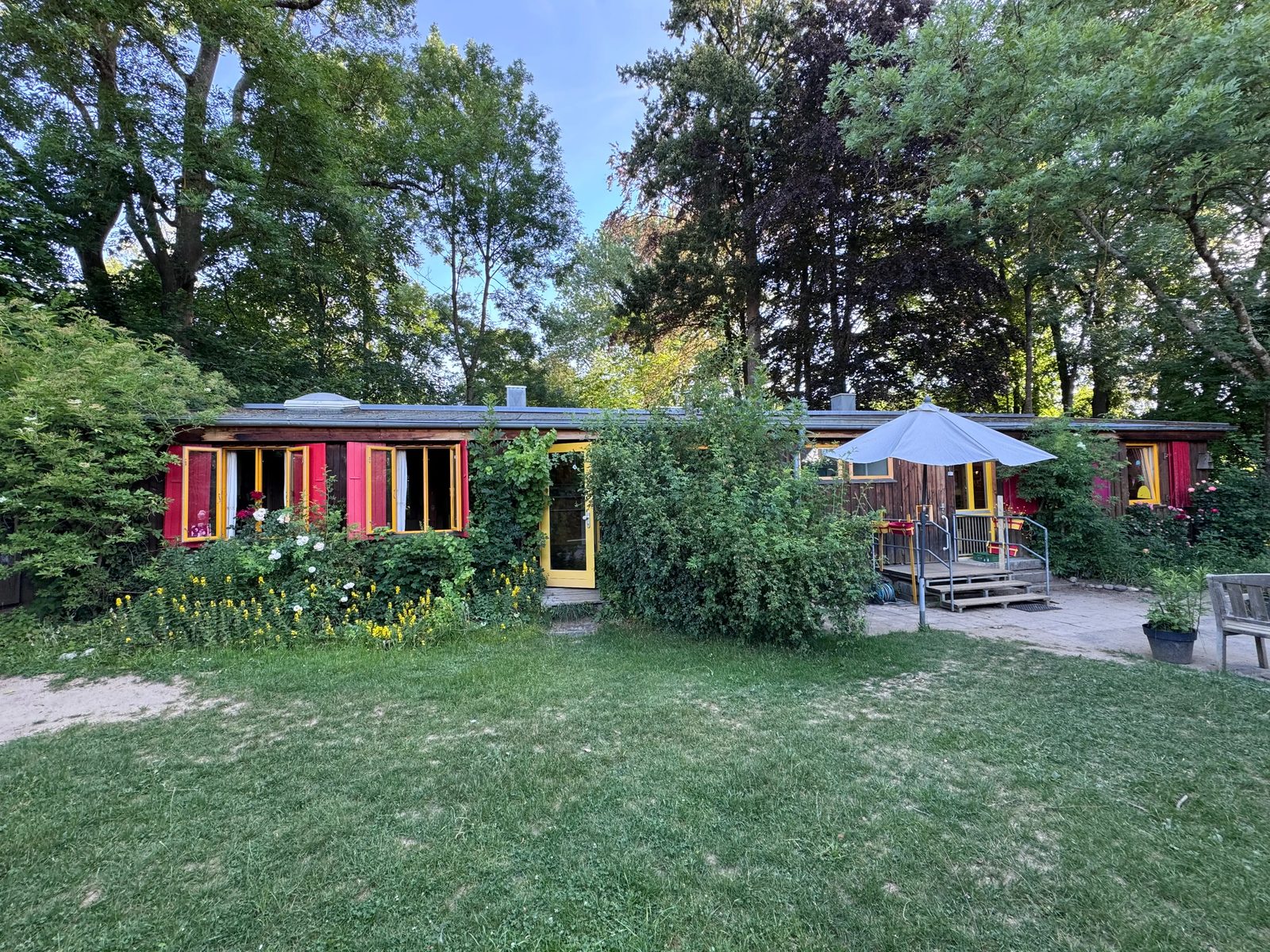 Das Kindergartenhaus aus Holz mit roten Fensterläden, davor der Garten